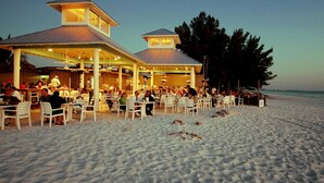 A beachfront restaurant with outdoor seating and a covered patio area.
