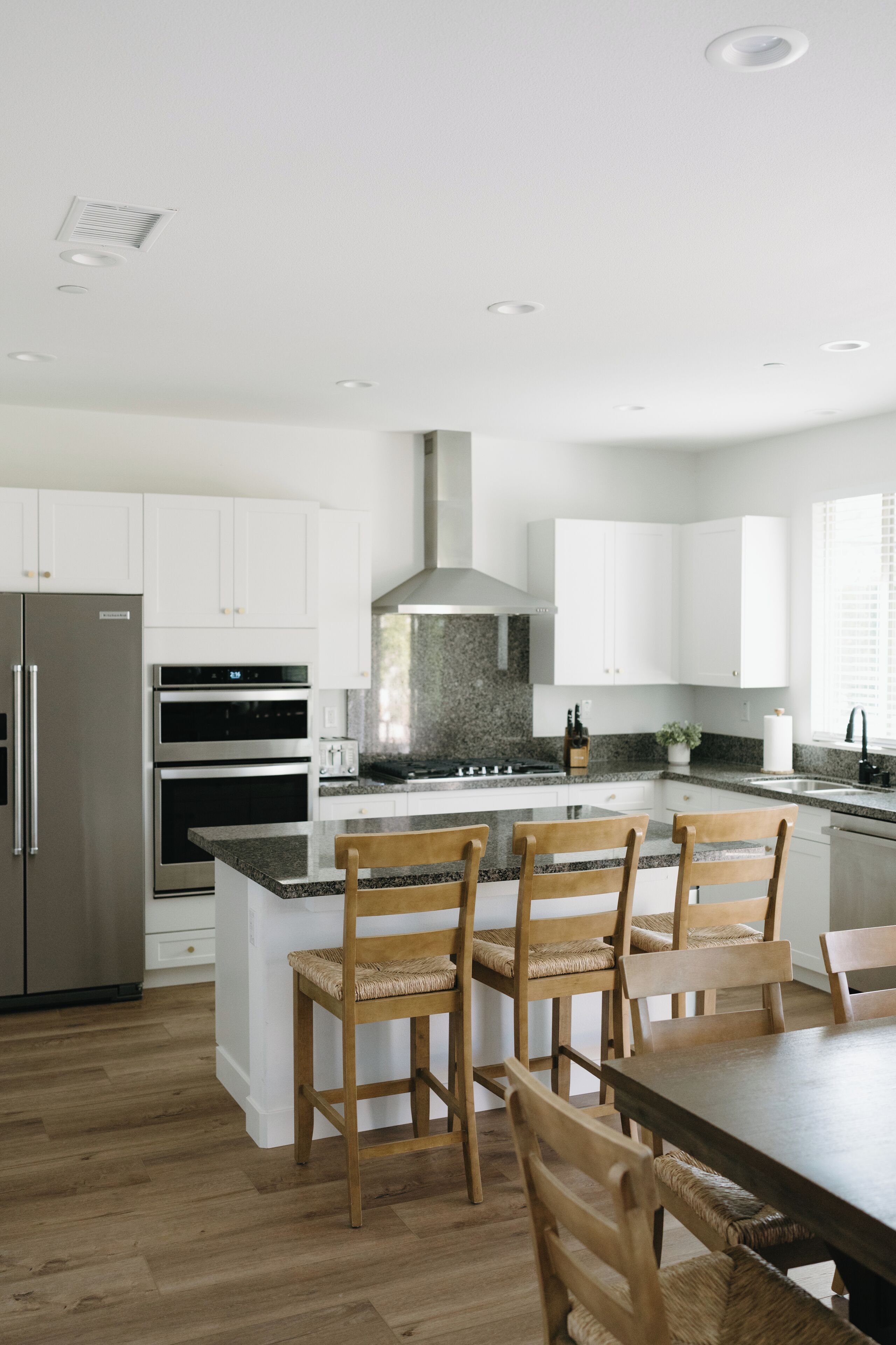 Une cuisine moderne avec des meubles blancs, des appareils en acier inoxydable et un îlot central doté de tabourets de bar.