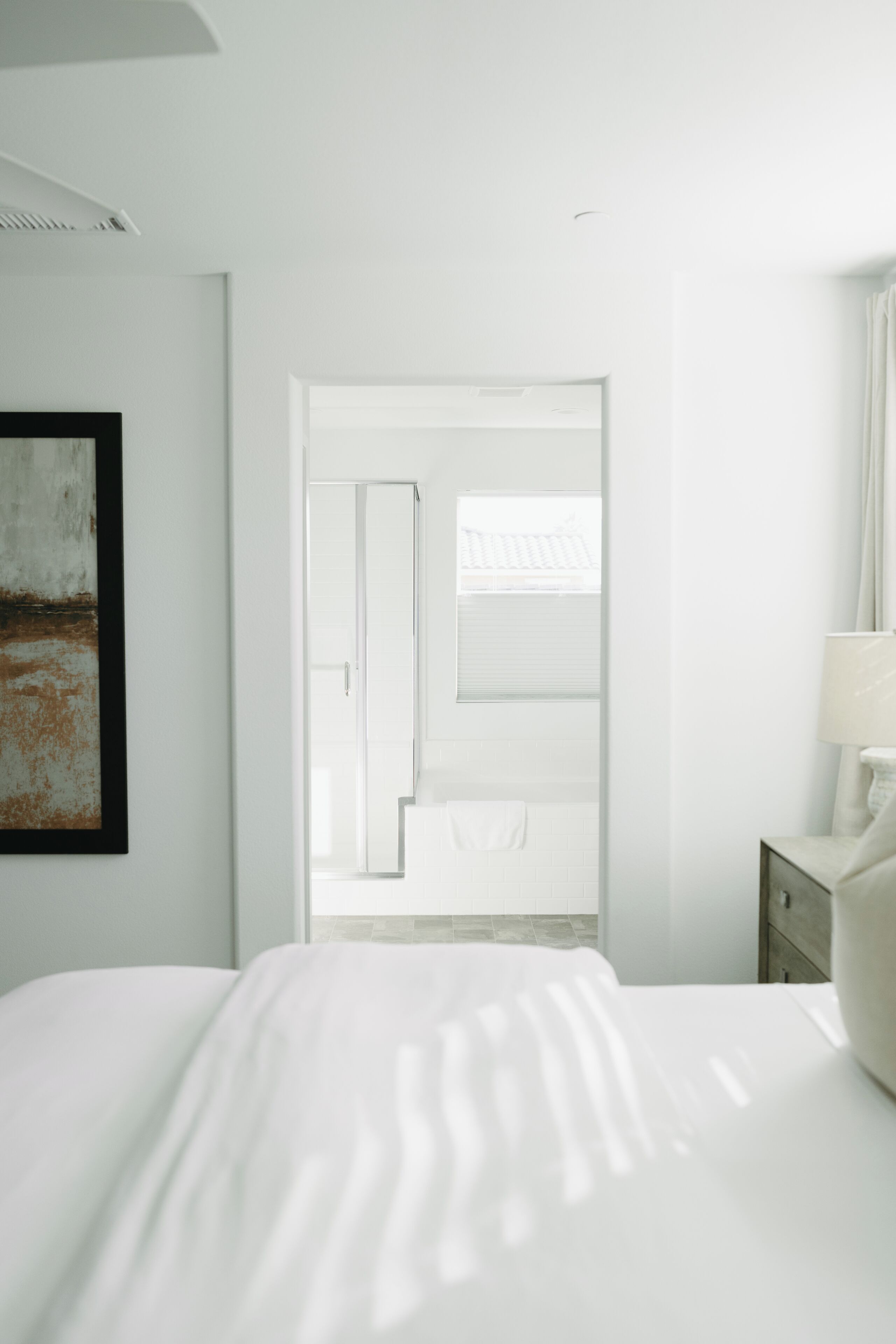 A modern hotel room with a large bed, a nightstand, a lamp, and a view of the outside through a door.