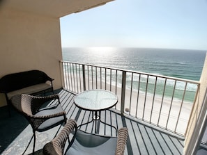 A balcony with a view of the ocean, a round table, and wicker furniture.