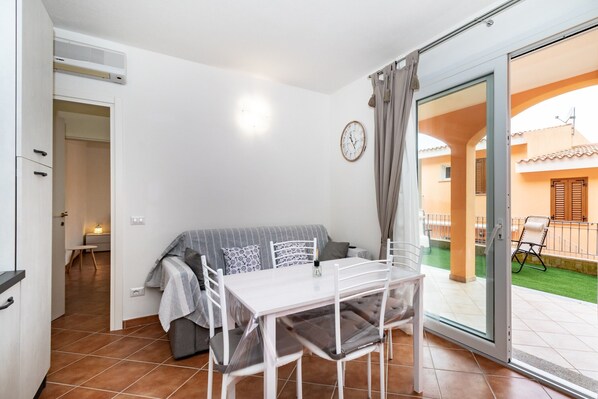 Una habitación con una mesa de comedor, sillas, un sofá, una puerta corrediza de vidrio a un espacio exterior y un ventilador de techo.