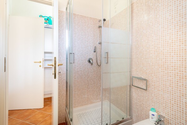 Un baño con cabina de ducha de vidrio, un lavamanos blanco y pared con azulejos.