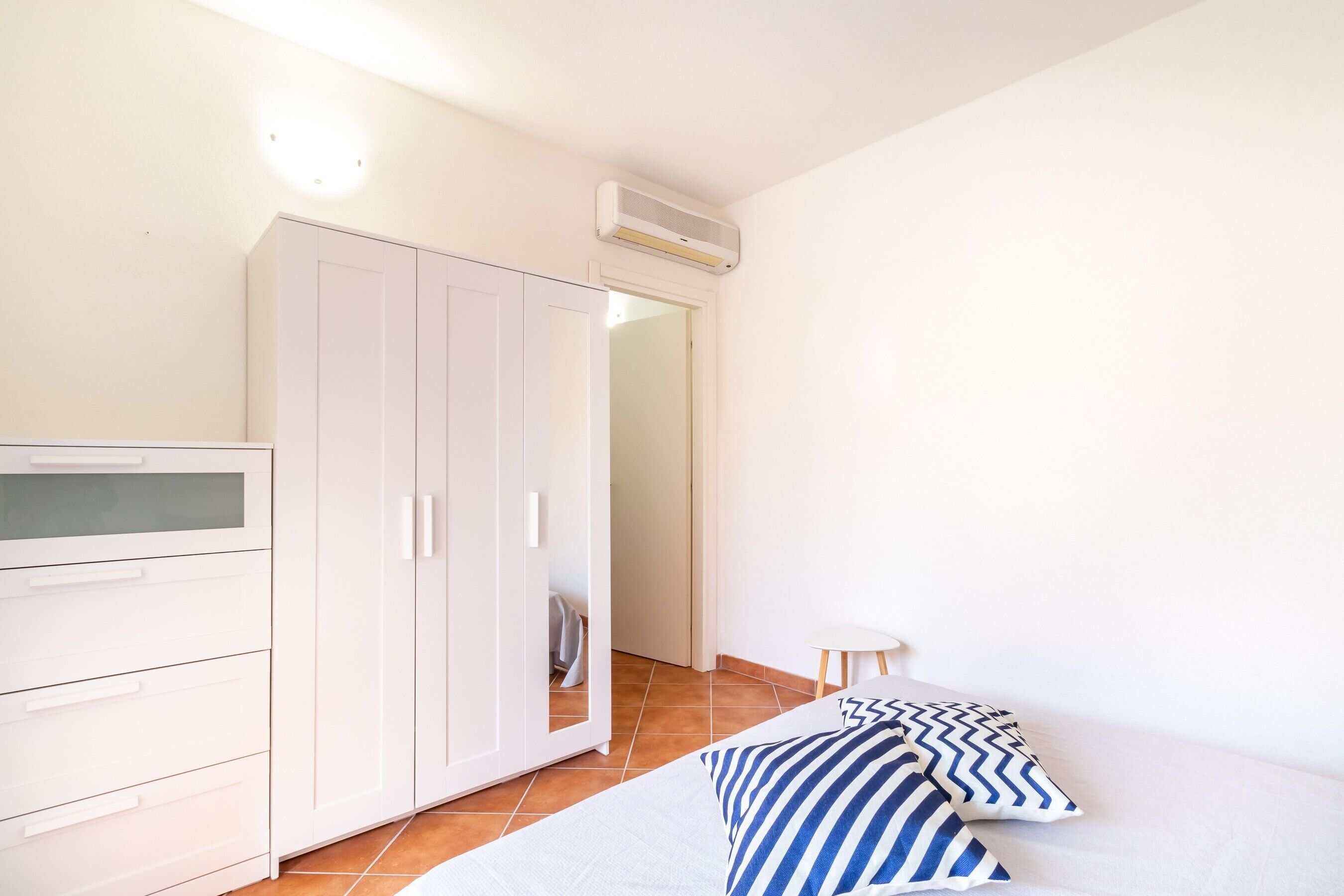 Un dormitorio con cama, armario, una mesita y aire acondicionado.