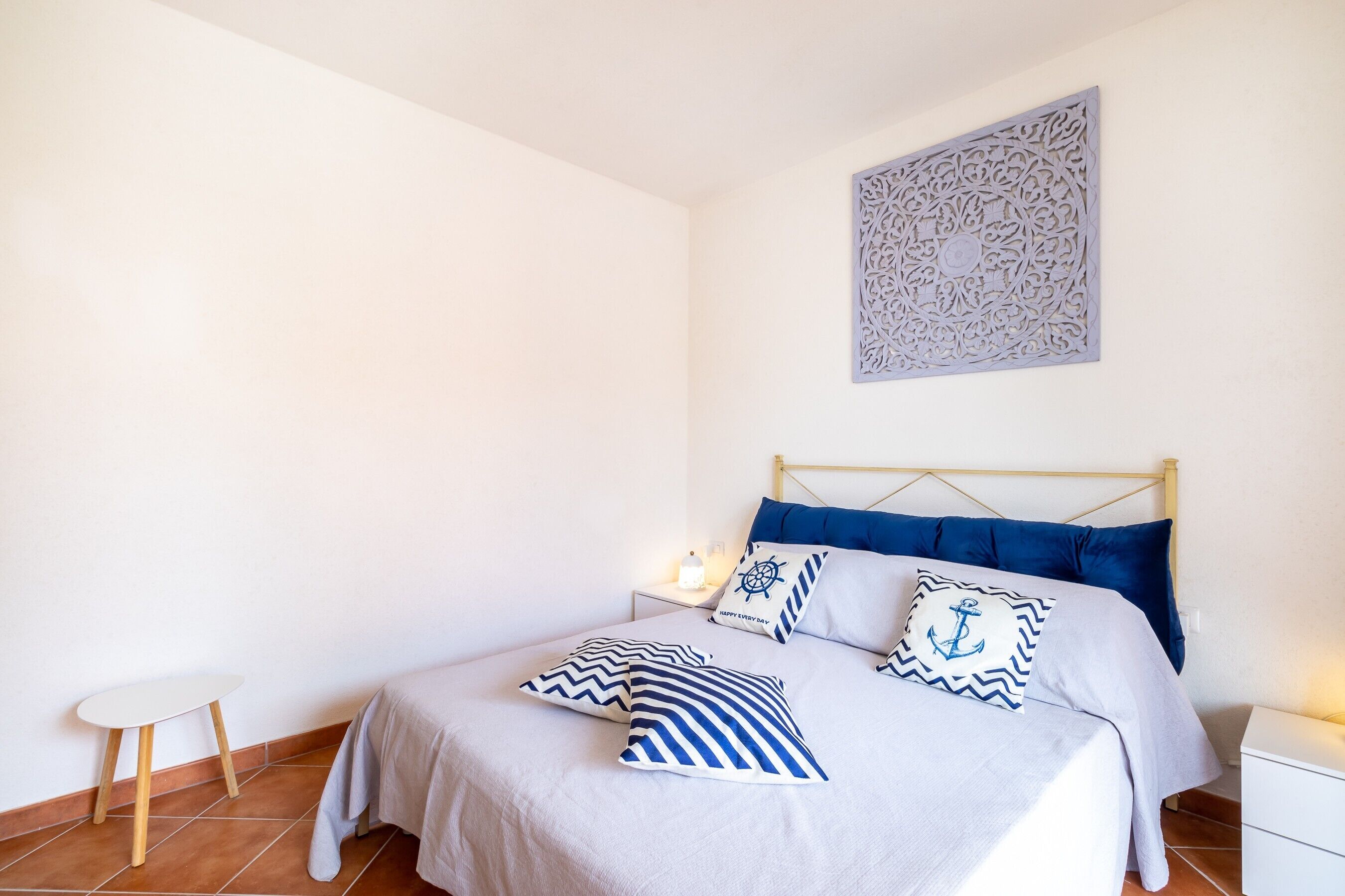 Une chambre à coucher bien aménagée, avec un lit, des tables de chevet, un élément décoratif fixé au mur et un sol carrelé.