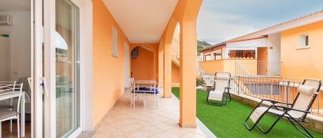 A balcony with a glass door, a table with chairs, and a grassy area with lounge chairs.