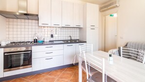 Una cucina moderna con mobili bianchi, un piano cottura a gas, forno e zona pranzo con tavolo e sedie.