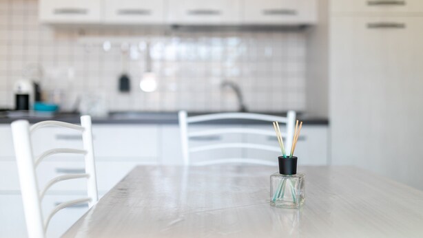 Una cucina moderna con mobili bianchi, zoccolo in piastrelle e un tavolo da pranzo con un vaso di vetro trasparente.