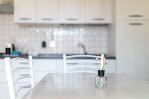 Una cocina moderna con armarios blancos, salpicadero de azulejos y una mesa de comedor con un jarrón de cristal transparente.