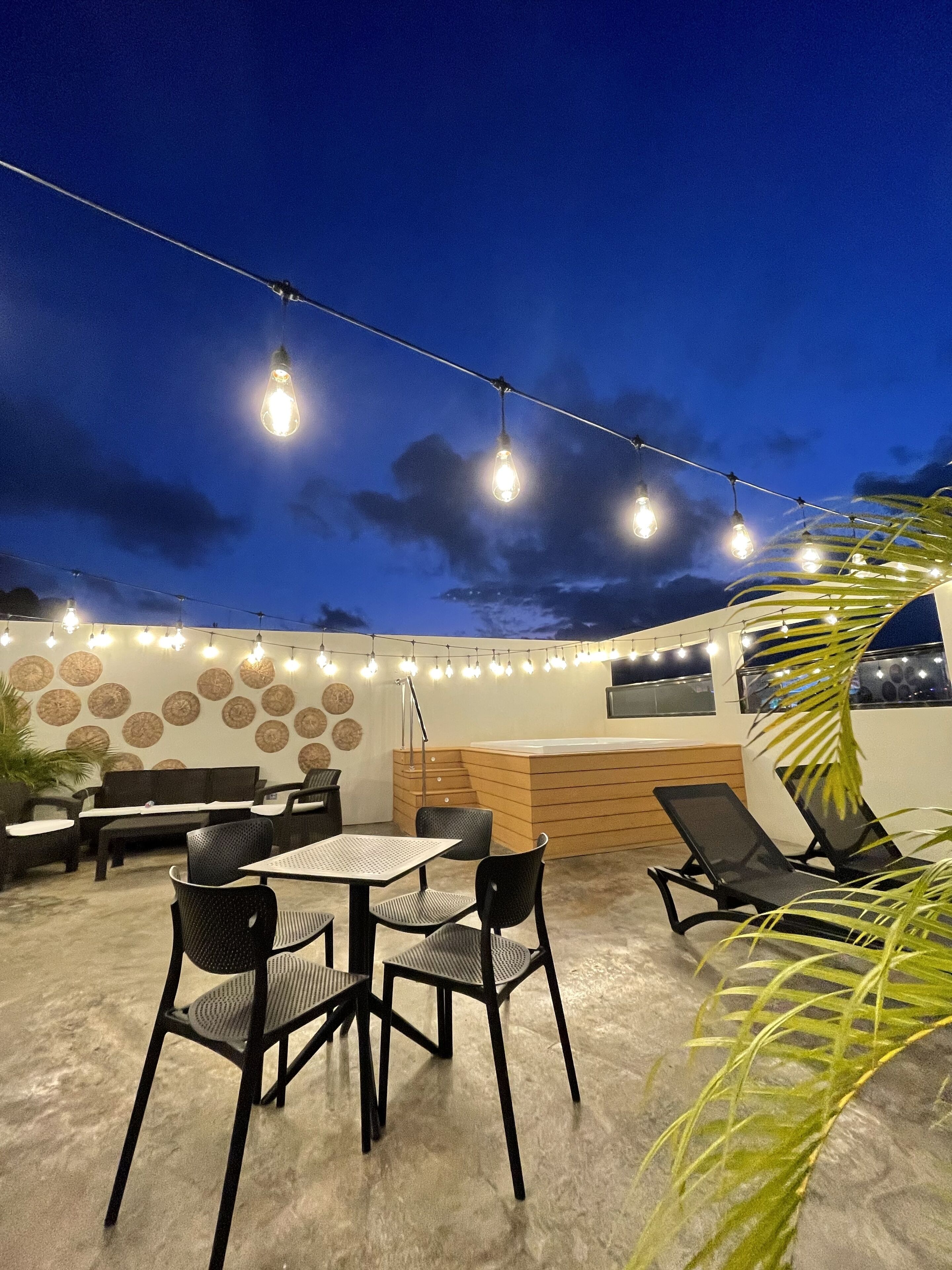 An outdoor seating area with tables and chairs, a wooden counter, and string lights.