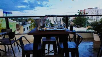 An outdoor dining area with a table and chairs, string lights overhead, and a view of buildings in the background.