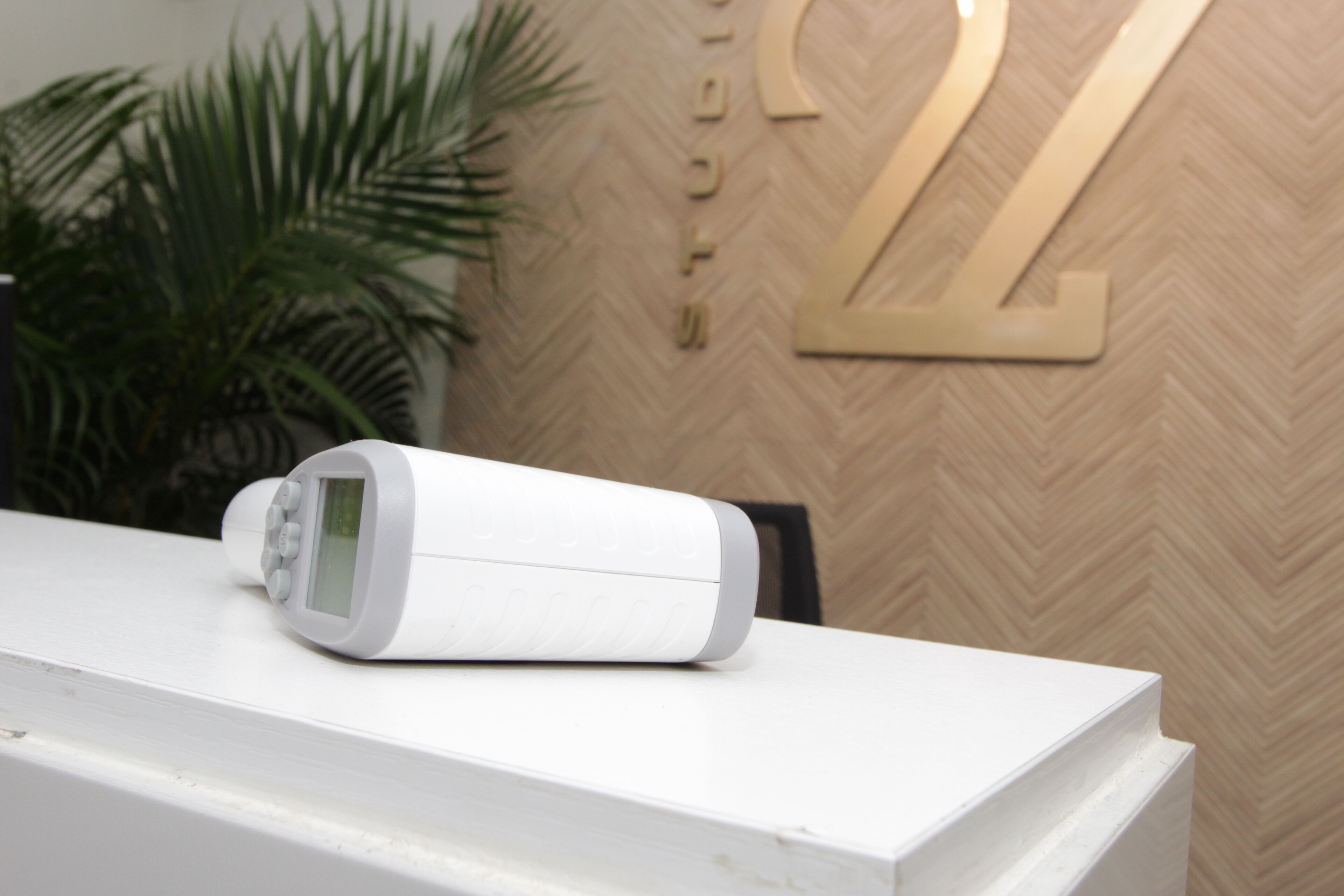 Un termostato digital blanco sobre una encimera blanca, con una pared de diseño en espiga al fondo.