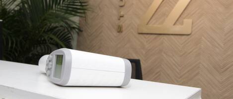 Un termostato digital blanco sobre una encimera blanca, con una pared de diseño en espiga al fondo.