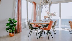 A dining area with a large table, chairs, and a view of the sea.