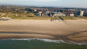 Vista aérea de una zona costera con playa arenosa, un barco pequeño y un pueblo al fondo.