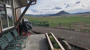 Un patio con mobiliario exterior, una parrilla de barbacoa y vistas a un campo cubierto de hierba y montañas.