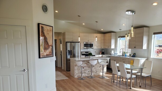 Una cocina moderna con una isla central, electrodomésticos de acero inoxidable y un comedor con sillas blancas.