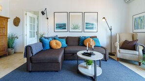 Ein Wohnzimmer mit einer Eckcouch, einem runden Couchtisch, einer Stehlampe und gerahmten Bildern an der Wand.