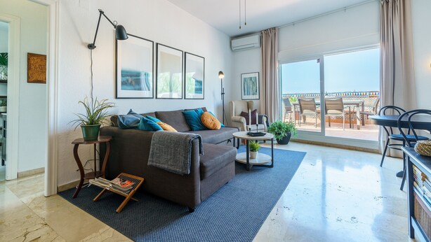 Ein modernes Wohnzimmer mit einer Couch, einem Couchtisch und einem Balkon mit Gartenmöbeln.