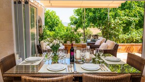 An outdoor dining area with wicker furniture, glass tables, and a view of greenery.
