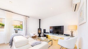 A modern living room with a sofa, a glass coffee table, a TV, a fireplace, and a dining area.