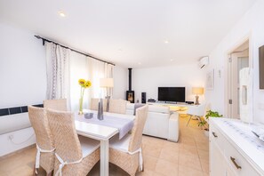 Una sala de estar moderna con comedor, muebles blancos, un televisor de pantalla plana y una chimenea.
