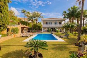 A pool surrounded by a well-maintained lawn, palm trees, and a two-story building with a balcony.