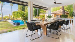 Et moderne udeområde med spiseplads, pool, stole og udsigt til en villa.