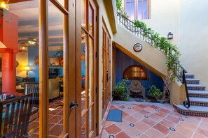 Un pasillo amplio con suelo de baldosas, una escalera con barandilla decorativa y vistas al interior.