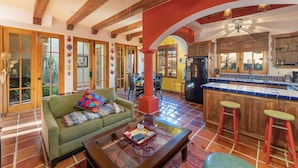 A spacious living room with a green sofa, a coffee table, and a kitchen area with a red column and wooden cabinets. - Casa Juanchi by Casago (Loreto)