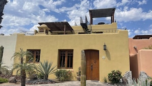 A two-story building with a flat roof, a wooden door, and a balcony with a pergola. - Casa Juanchi by Casago (Loreto)