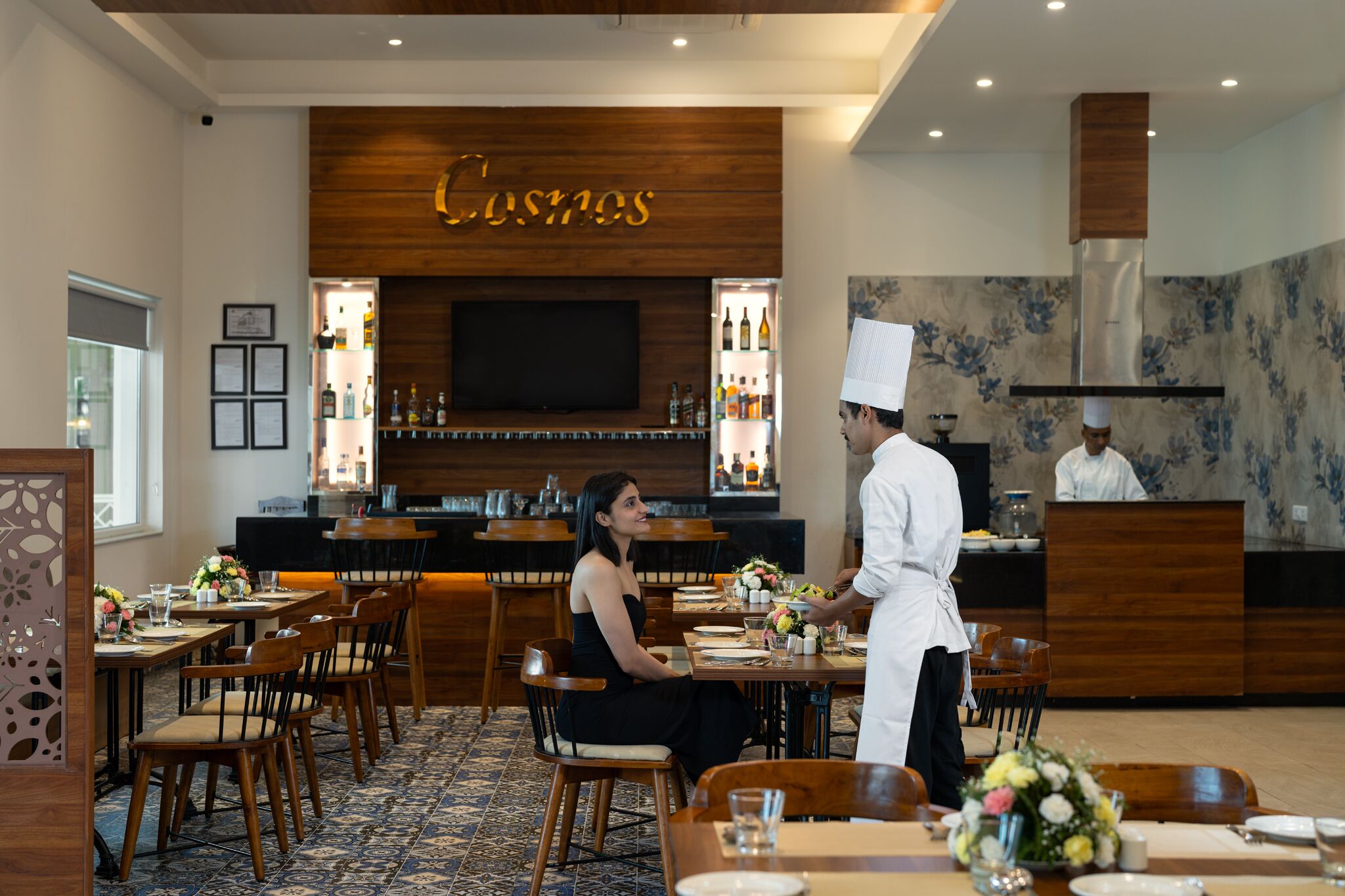 A restaurant with wooden decor, a bar area, and a chef serving a guest.