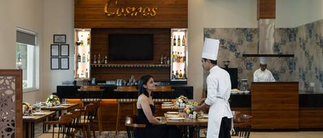 A restaurant with wooden decor, a bar area, and a chef serving a guest.