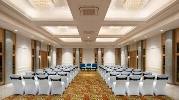 Une salle de conférence avec des rangées de chaises blanches, une moquette à motifs, des lustres et un canapé bleu.