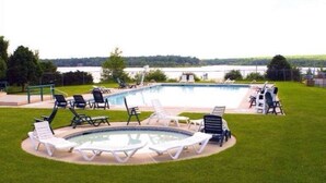 Une piscine dotée de chaises longues et d’un espace avec bain à remous, le tout entouré d’une pelouse bien entretenue et offrant une vue sur un lac.