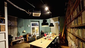 A cozy, well-lit room with a wooden table, chairs, a bookshelf, and a radiator. - JC&BLUE Guesthouse - Hostel (Frankfurt)