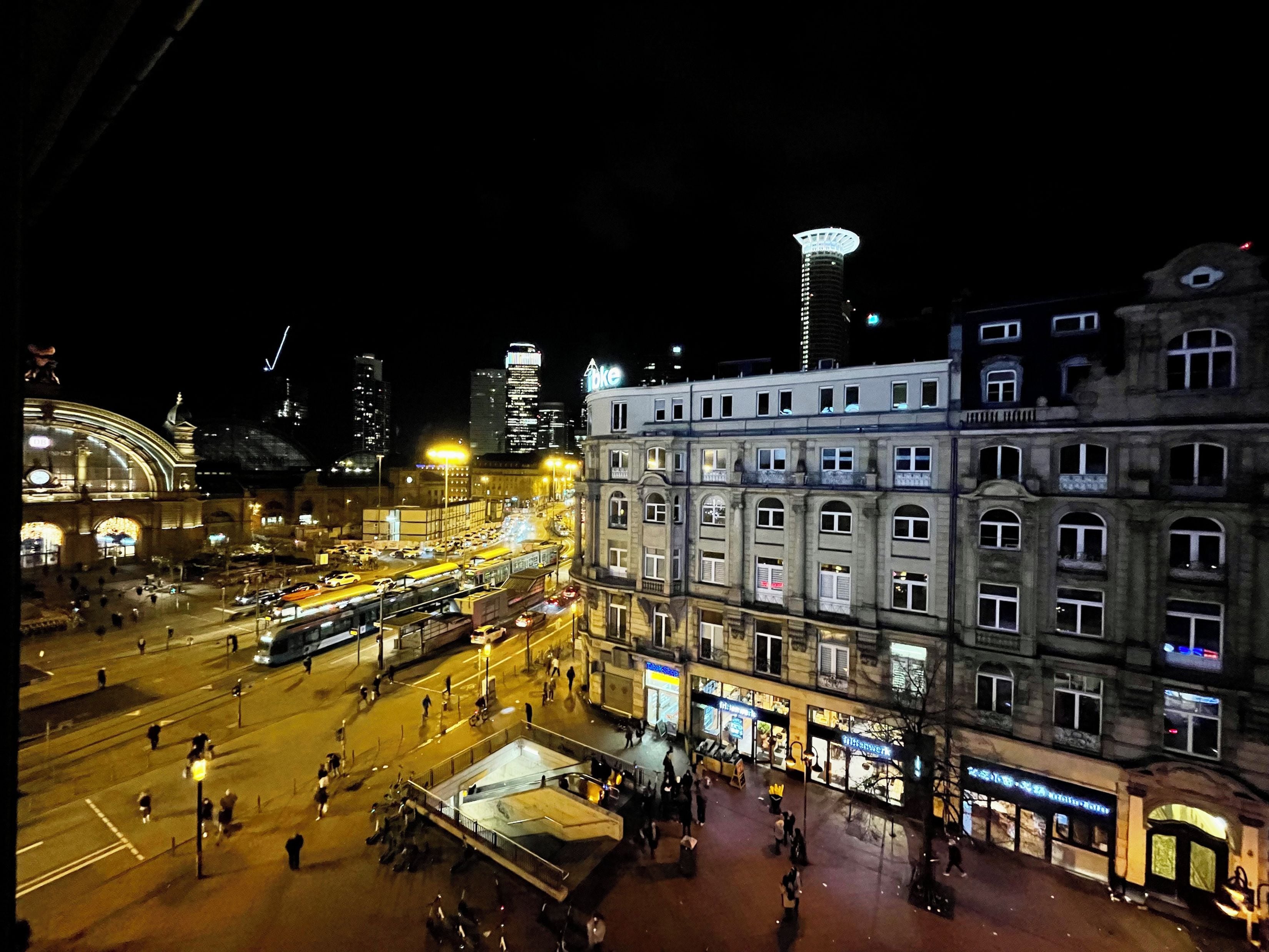 Un paisaje urbano nocturno con un edificio destacado que tiene múltiples ventanas y una plaza central abierta.