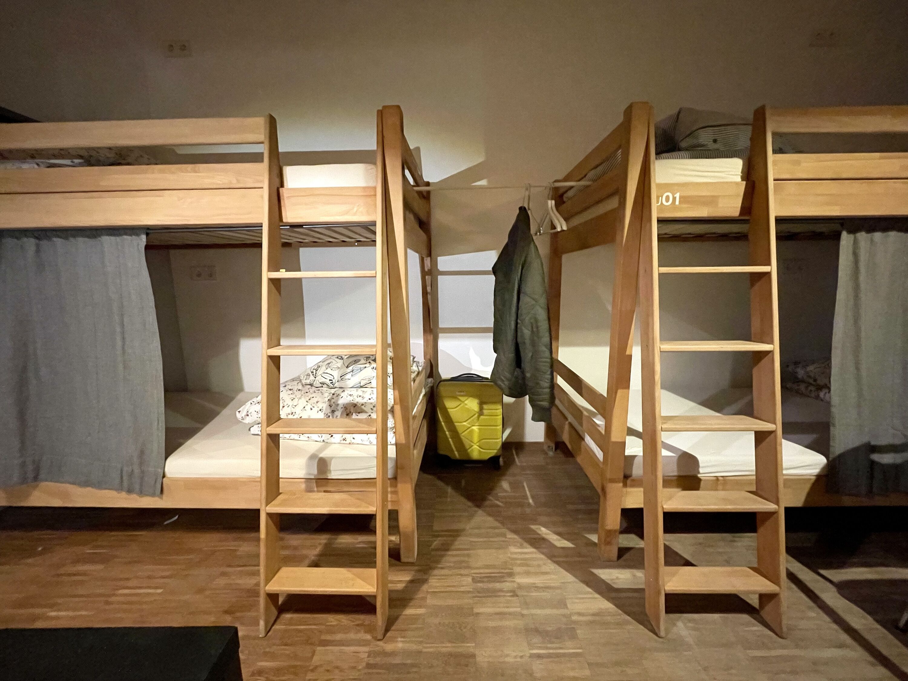 A bunk bed room with wooden ladders, a yellow storage box, and a jacket hanging on the ladder.