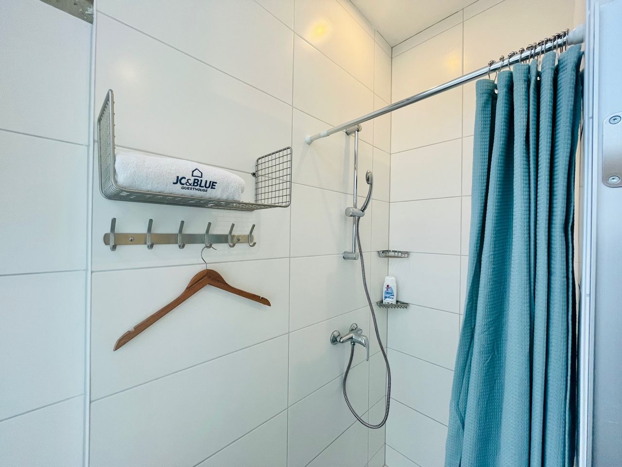 A bathroom with a shower, a towel rack with a towel, a hanging wooden hanger, and a shower curtain.