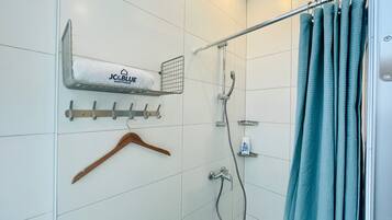 A bathroom with a shower, a towel rack with a towel, a hanging wooden hanger, and a shower curtain.