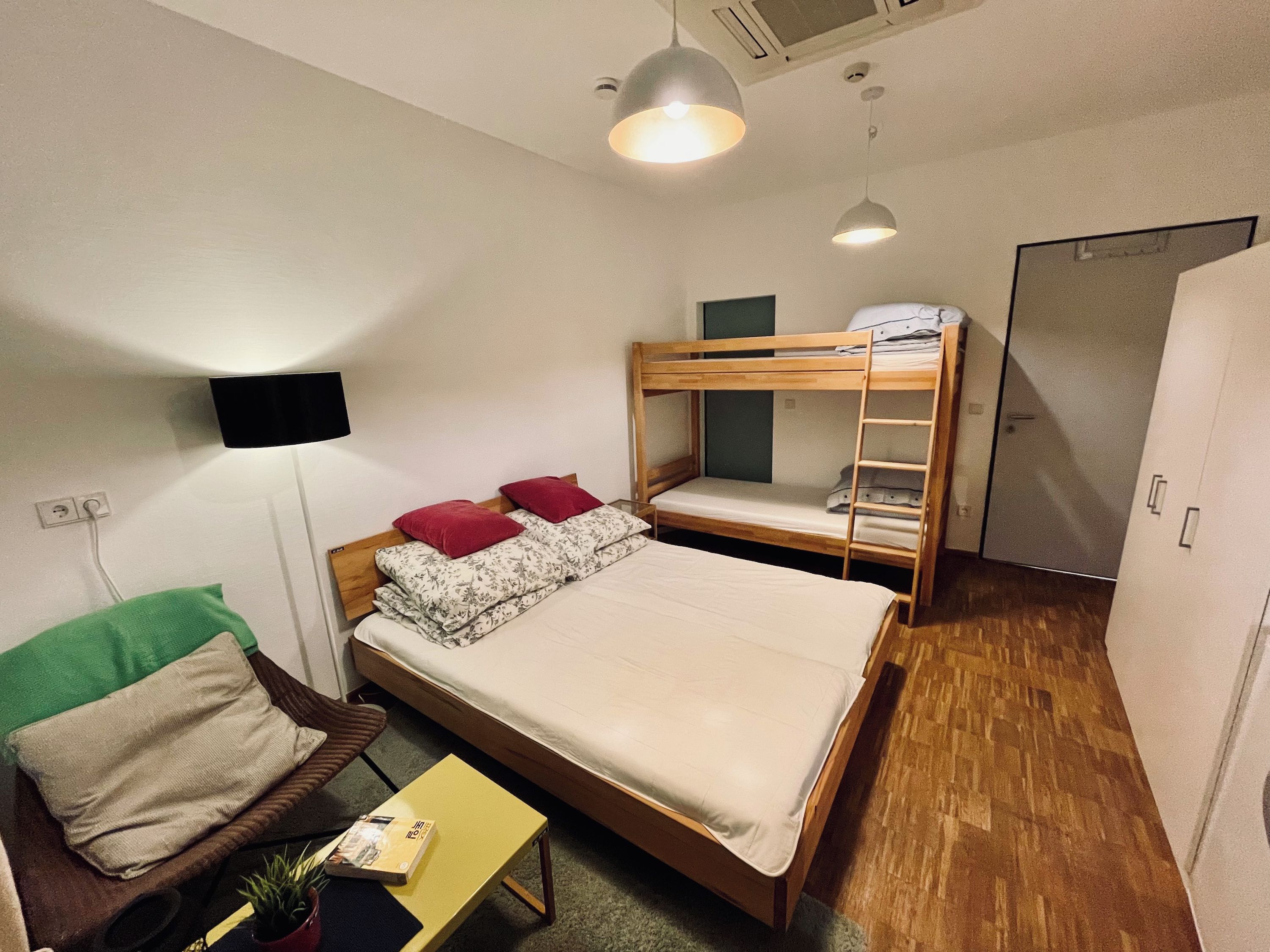 A compact hotel room with a bunk bed, a single bed, a small table with a plant, a TV mounted on the wall, and a wardrobe.