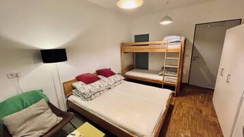 A compact hotel room with a bunk bed, a single bed, a small table with a plant, a TV mounted on the wall, and a wardrobe.