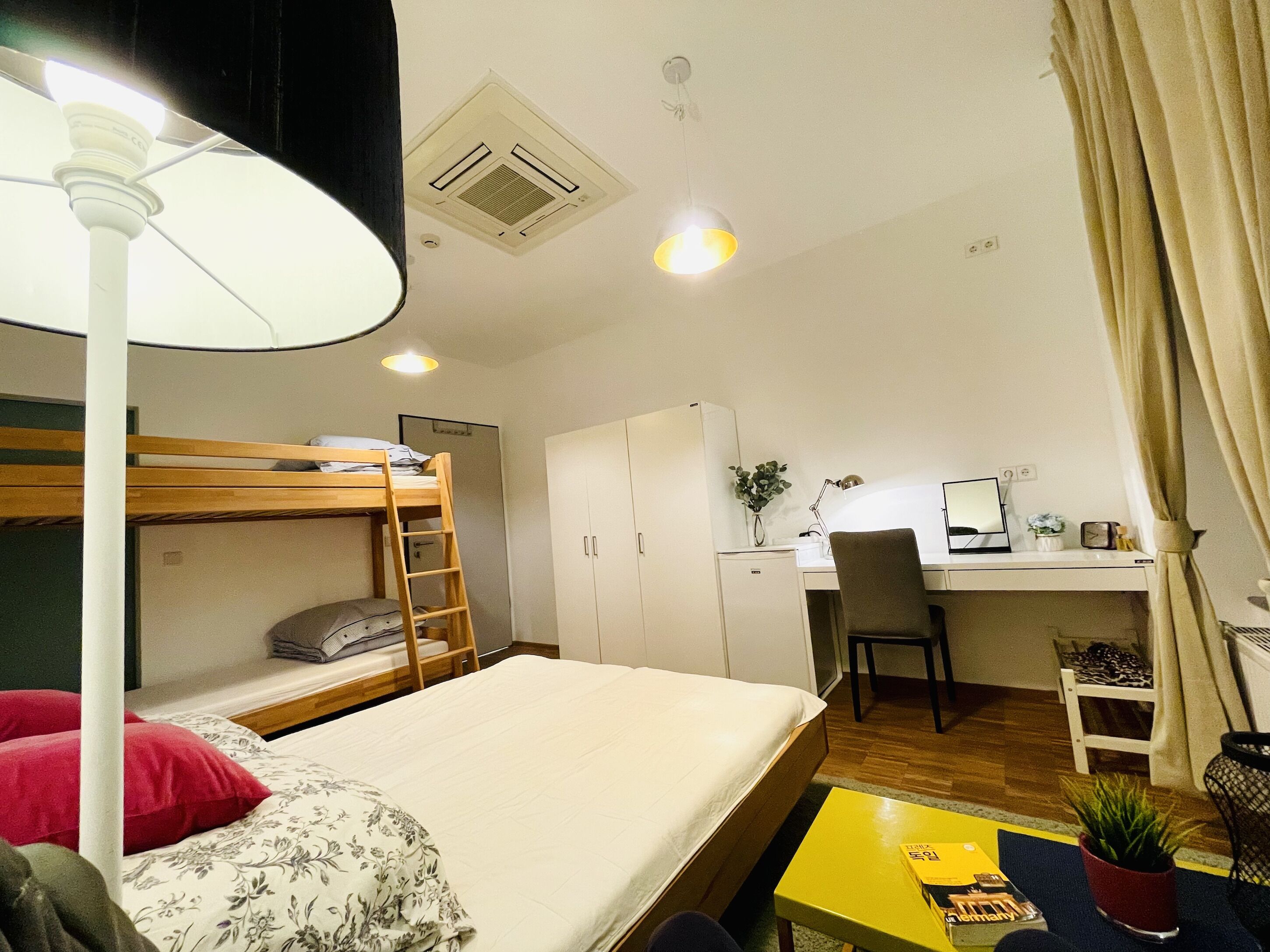 Una habitación compacta con una cama litera, un escritorio con silla, una mesita pequeña y una planta en maceta.