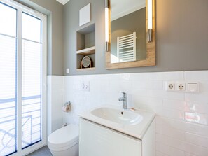 A bathroom with a toilet, sink, mirror, and a window with blinds.