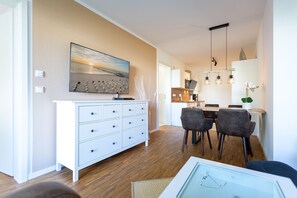 Ein modernes Wohnzimmer mit einem weißen Schrank, einer Essecke mit Tisch und Stühlen sowie einer Küche im Hintergrund.