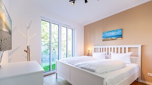 Un dormitorio moderno con una cama grande, un escritorio y vistas a la vegetación a través de una puerta corrediza.
