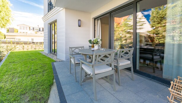 Un patio con una mesa y sillas, un pequeño jardín y un puerta de vidrio que da a un espacio interior.
