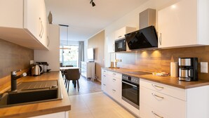 Una cocina moderna con microondas, horno y lavadero integrados. Se observa un comedor con mesa y sillas al fondo.