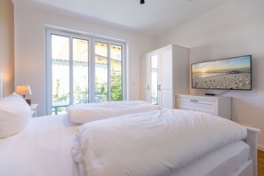 Ein Schlafzimmer mit zwei Betten, einem Fernseher und einem großen Fenster mit Blick auf Grünflächen.