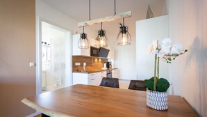 Un comedor con una mesa de madera, sillas e iluminación colgante. Hay una orquídea en maceta sobre la mesa.