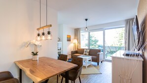 Una sala de estar moderna con una mesa de comedor de madera, sillas de cuero, un sofá y una mesa de centro de vidrio. Hay una ventana grande con cortinas, una lámpara y una planta sobre la mesa.